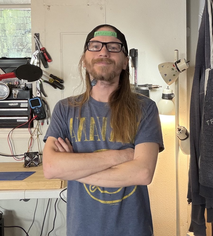 Tj, the shop's technician, arms crossed at the bench in Longmont
