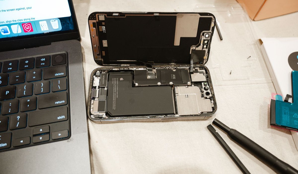 Illustrative photo: a phone opened for repair on a bench with tools and a laptop